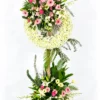 Dawn pink gerbera funeral wreath stand with white mums, lilies, orchids and a flower base