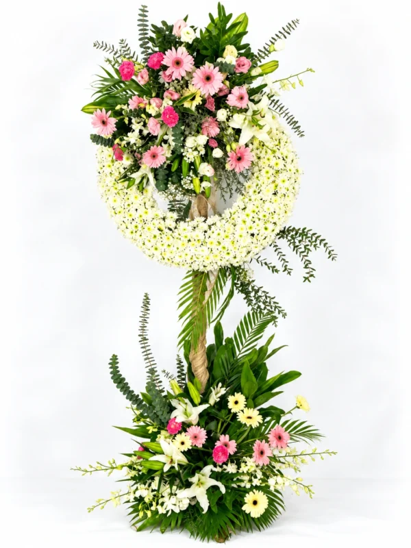 Dawn pink gerbera funeral wreath stand with white mums, lilies, orchids and a flower base