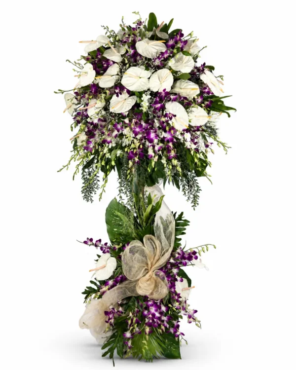 White anthurium and purple dendrobium orchid two-layer funeral stand with eucalyptus, tropical leaves and a cream abaca bow